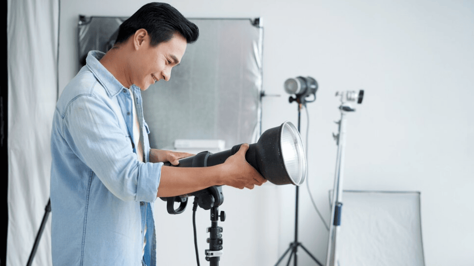 一名男子在摄影棚中调整灯光设备，展现摄影学院的专业实践环境。